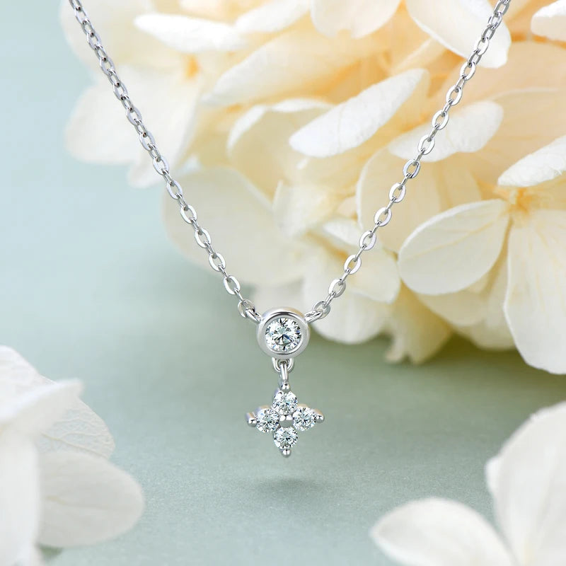 four leaf clove moissanite necklace in white gold plated silver on a light green background with flowers