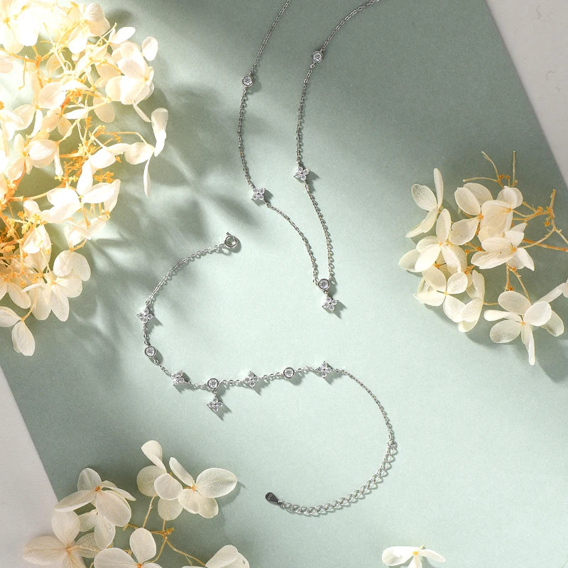 four leaf clove moissanite bracelet and  necklace in white gold plated silver on a light green background with flowers